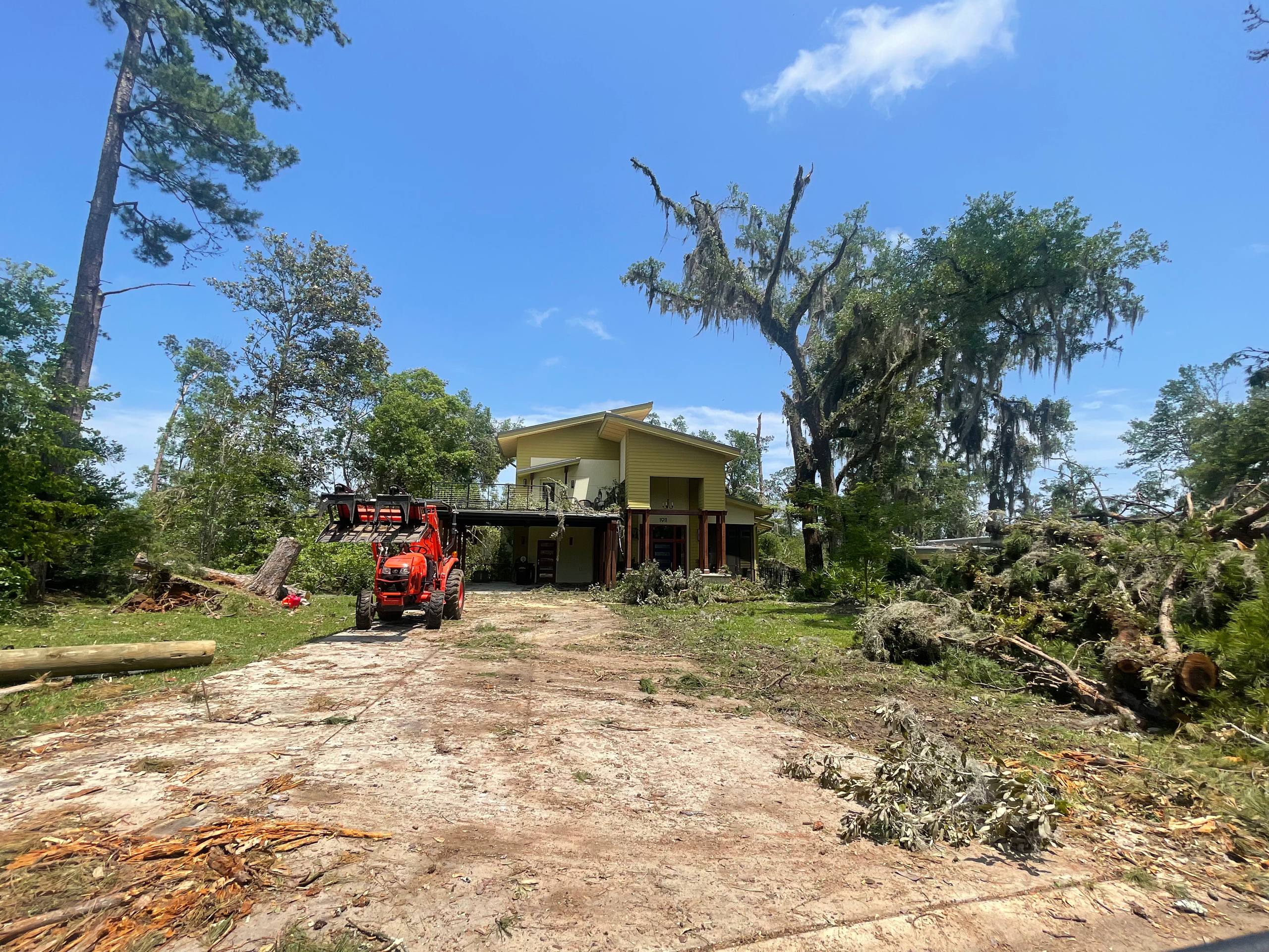 Orange loader on a cleared driveway beside a debris pile