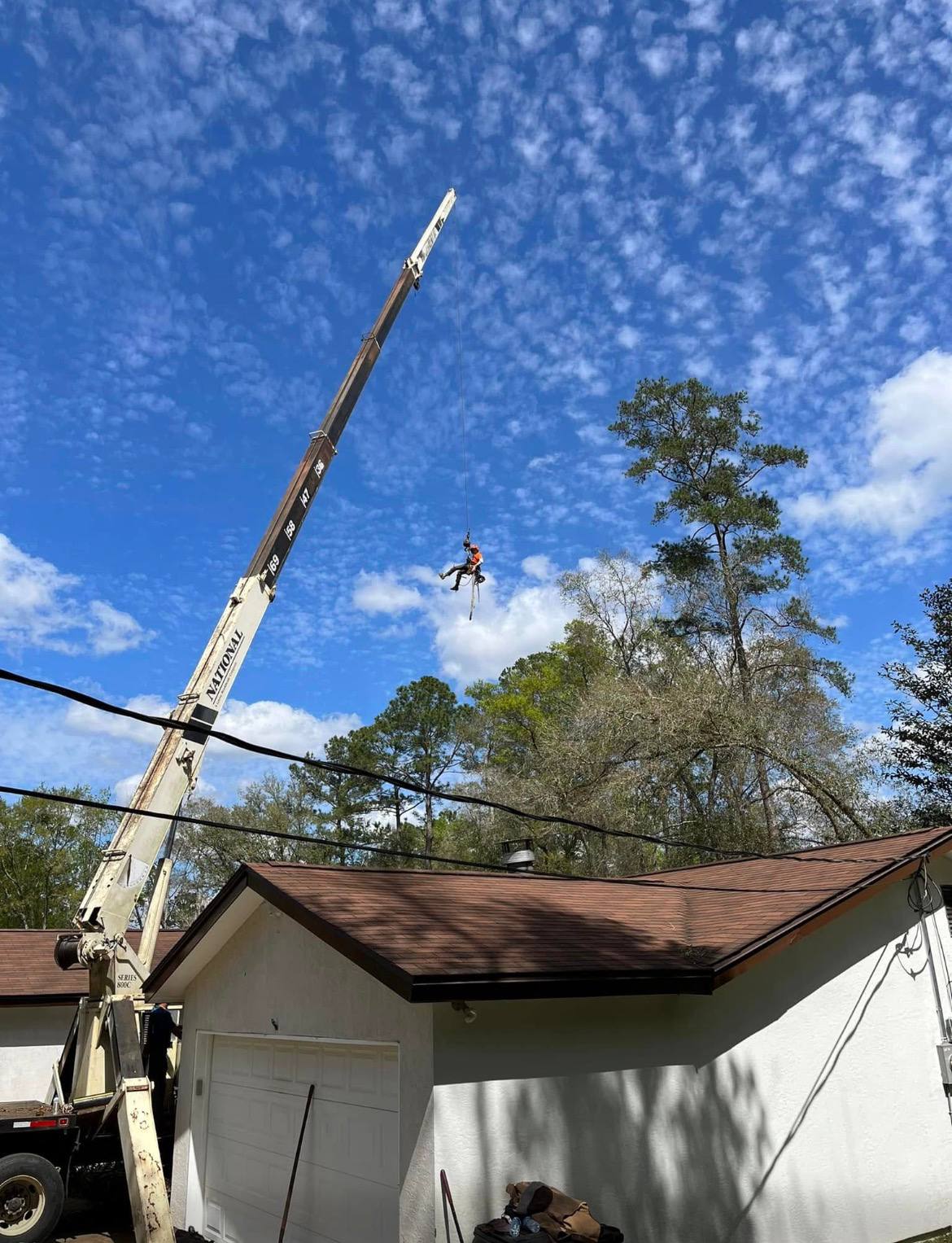 Crane lifting tree sections over residential roof in Tallahassee FL